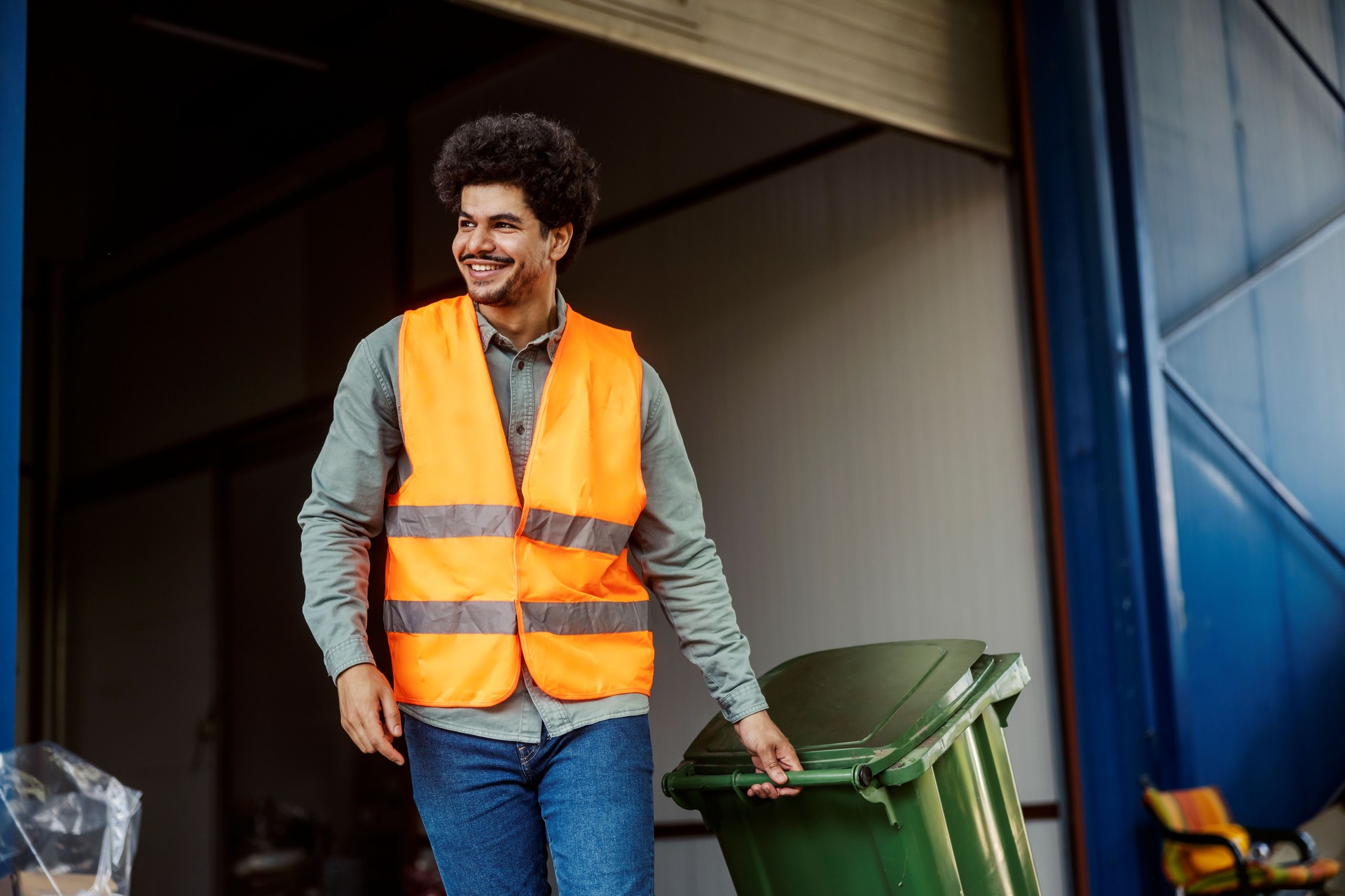 Smiling multicultural warehouse worker taking out trash.